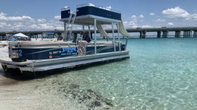 A blue double-decker pontoon boat with slides docked on the beach in Destin, Florida