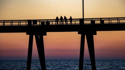 a group of people walking over a bridge in the sunset