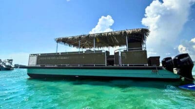 A pontoon boat with a thatched roof floats on clear turquoise water under a sunny sky.